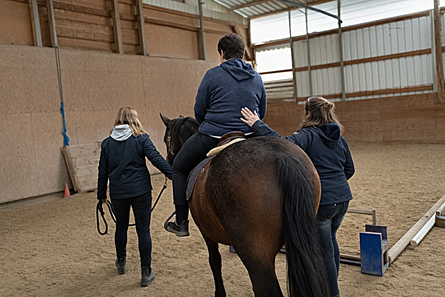Hippotherapie-Sitzung mit Patient*in, Physiotherapeut*in und Pferdefuehrer*in in der Reithalle