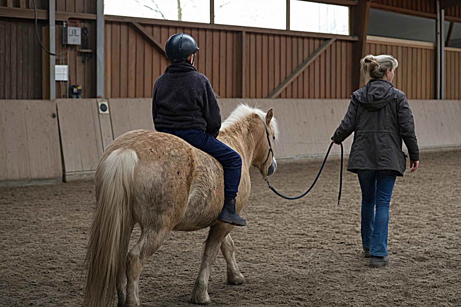 Kind sitzt entspannt auf dem Rücken eines Therapie-Ponys an der Longe, begleitet von einer Reittherapeutin